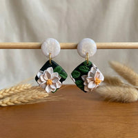 White Lotus handmade polymer-clay earrings, displayed on a stand in soft daylight