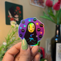 Masked Spirit vinyl sticker, flat-lay showing holographic round sticker with masked spirit and small dark spirit figures on purple background