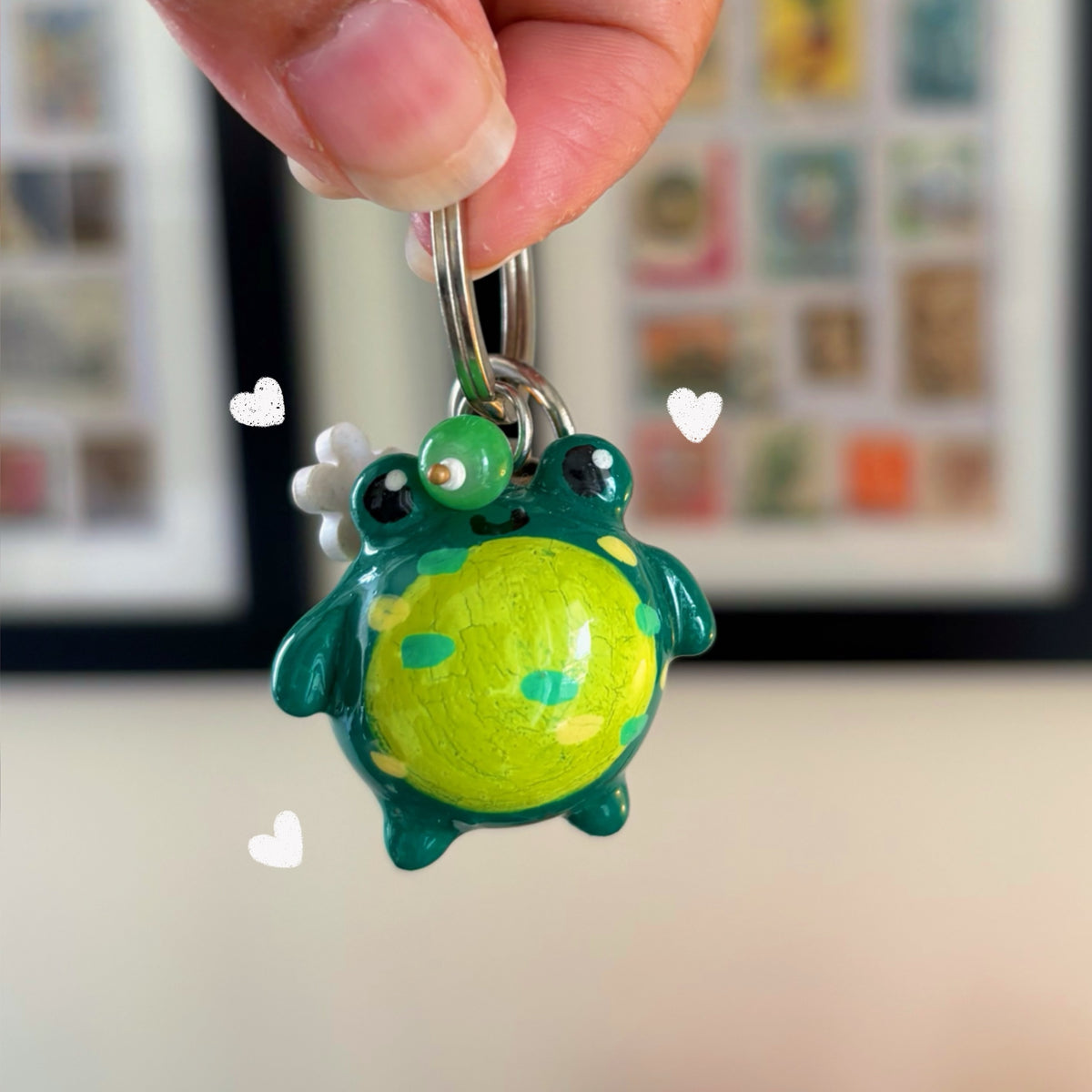 Froggy handmade polymer clay keychain, chubby green frog with yellow-green belly and teal spots, white daisy clip, on silver ring