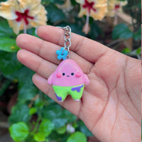Pink Starfish handmade polymer clay keychain, pink triangular character with lime green shorts, held in hand, blue flower charm