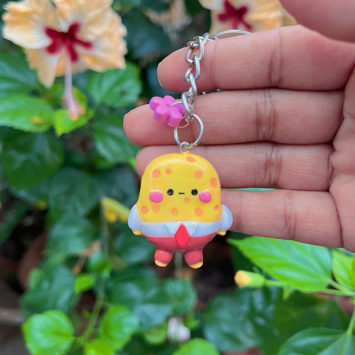 Yellow Sponge handmade polymer clay keychain, yellow spotted square character with red pants, held in hand among hibiscus flowers