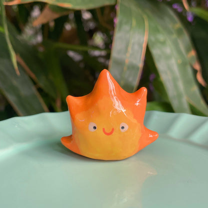 Flame Spirit handmade polymer clay keychain, orange and yellow flame-shaped character with smiling face, glossy glaze, on mint plate