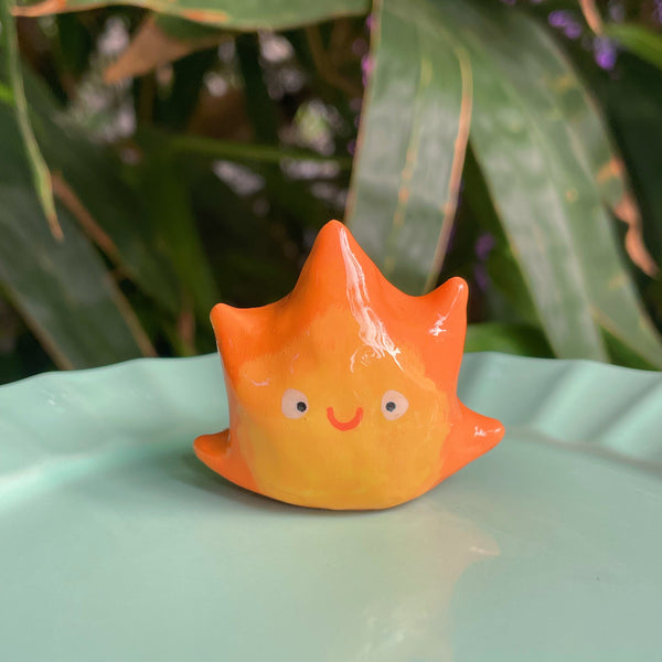 Flame Spirit handmade polymer clay keychain, orange and yellow flame-shaped character with smiling face, glossy glaze, on mint plate