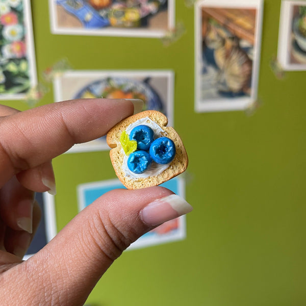 Blueberry ricotta toast handmade polymer clay keychain, miniature toast slice with blueberries and cream, held between fingers