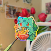 Seed Dinosaur ramen vinyl sticker, holographic flat-lay showing green dinosaur with seed bulb eating from ramen bowl
