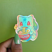 Seed Dinosaur ramen holographic vinyl sticker, illustrated teal green dinosaur with seed bulb eating ramen, die-cut shape, held in hand