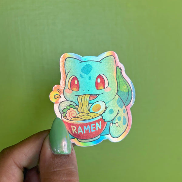 Seed Dinosaur ramen holographic vinyl sticker, illustrated teal green dinosaur with seed bulb eating ramen, die-cut shape, held in hand