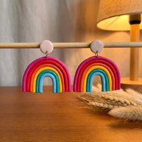 Rainbow handmade polymer-clay earrings, displayed on a stand in warm evening light