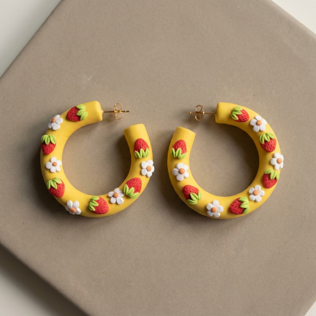 Strawberry Hoops handmade polymer-clay earrings, the pair on a warm stone surface