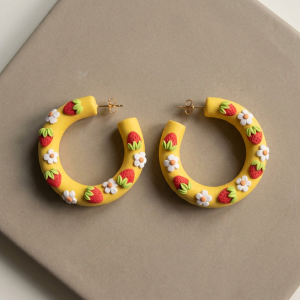 Strawberry Hoops handmade polymer-clay earrings, the pair on a warm stone surface