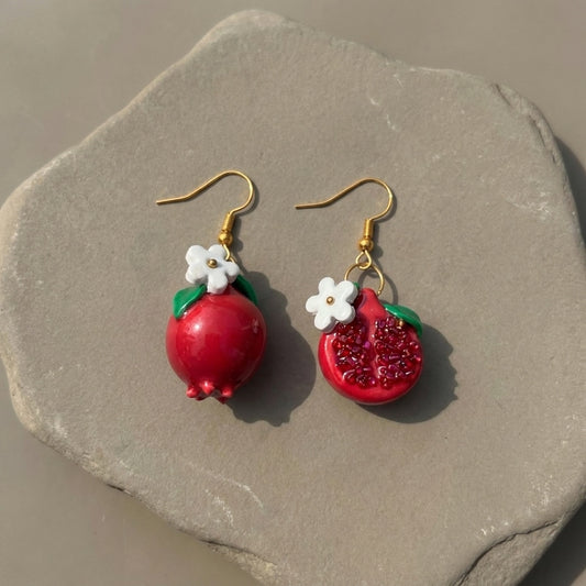 Pomegranates handmade polymer-clay earrings, the pair on a warm stone surface
