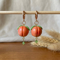 Peaches handmade polymer-clay earrings, displayed on a stand in soft daylight