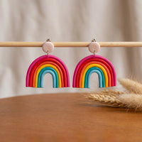Rainbow handmade polymer-clay earrings, displayed on a stand in soft daylight