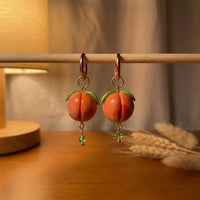 Peaches handmade polymer-clay earrings, displayed on a stand in warm evening light