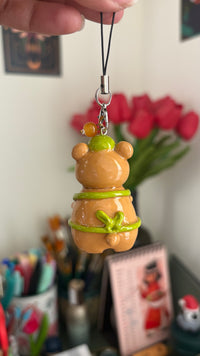 Bearista keychain polymer clay charm, back view showing green apron bow and amber bead on the silver clasp