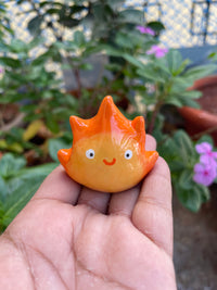 Flame Spirit polymer clay keychain, in-hand scale shot showing glossy orange flame figure with cute rosy expression