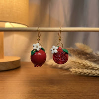 Pomegranates handmade polymer-clay earrings, displayed on a stand in warm evening light