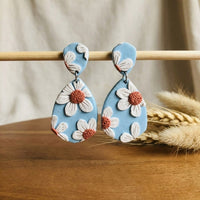 Daisy Blue handmade polymer-clay earrings, displayed on a stand in soft daylight