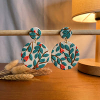 Teal Forest handmade polymer-clay earrings, displayed on a stand in warm evening light