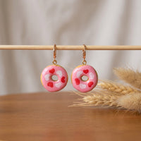 Donut Hearts handmade polymer-clay earrings, displayed on a stand in soft daylight