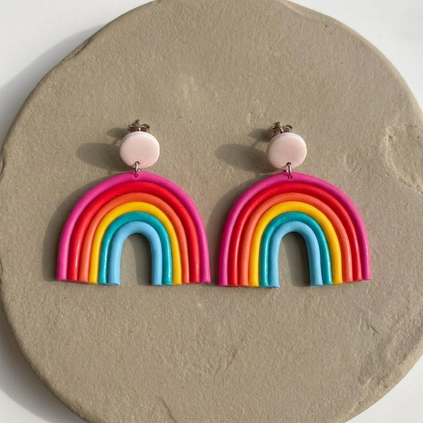 Rainbow handmade polymer-clay earrings, the pair on a warm stone surface
