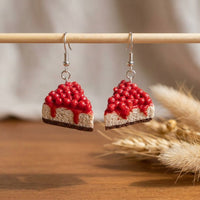 Cherry Cheesecake handmade polymer-clay earrings, displayed on a stand in soft daylight