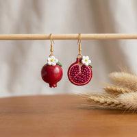 Pomegranates handmade polymer-clay earrings, displayed on a stand in soft daylight