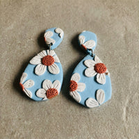 Daisy Blue handmade polymer-clay earrings, the pair on a warm stone surface