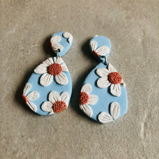 Daisy Blue handmade polymer-clay earrings, the pair on a warm stone surface