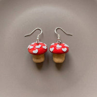 Shroom hearts handmade polymer-clay earrings, the pair on a warm stone surface