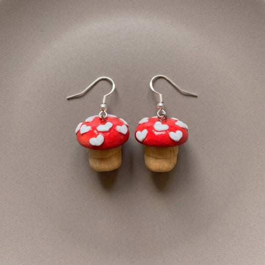 Shroom hearts handmade polymer-clay earrings, the pair on a warm stone surface