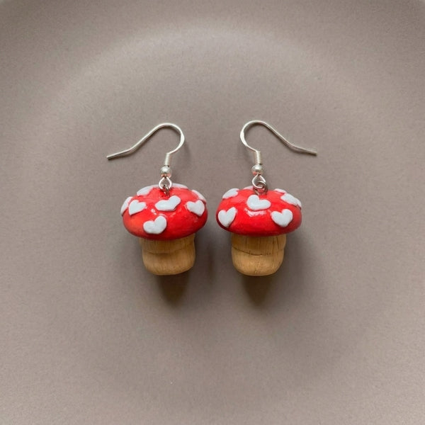 Shroom hearts handmade polymer-clay earrings, the pair on a warm stone surface