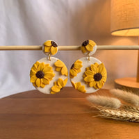Sunflower Dangles handmade polymer-clay earrings, displayed on a stand in warm evening light
