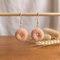 Sugar Donuts handmade polymer-clay earrings, displayed on a stand in soft daylight