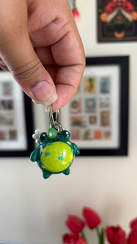 Froggy polymer clay keychain, in-hand close-up showing glossy green frog with spotted belly and daisy charm