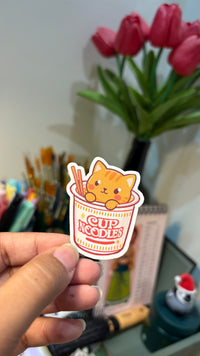 Ginger Kitty Noodles vinyl sticker held in hand, angled view showing the die-cut white border