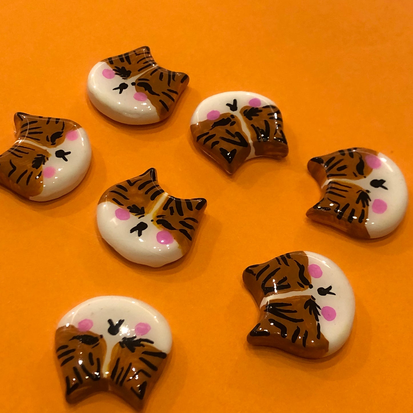 Lilly Poo polymer clay fridge magnet, in-hand scale shot showing orange cat face magnet with glossy glaze