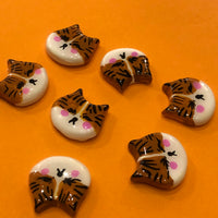 Lilly Poo polymer clay fridge magnet, in-hand scale shot showing orange cat face magnet with glossy glaze