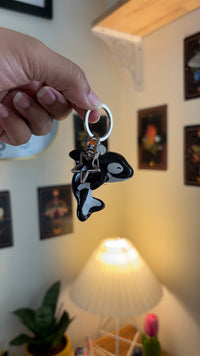 Orca polymer clay keychain, in-hand scale showing glossy black orca with white patches and silver ring clasp